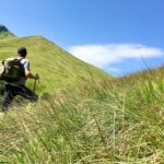A hiker trekking through lush green hills under a clear blue sky in Italy.