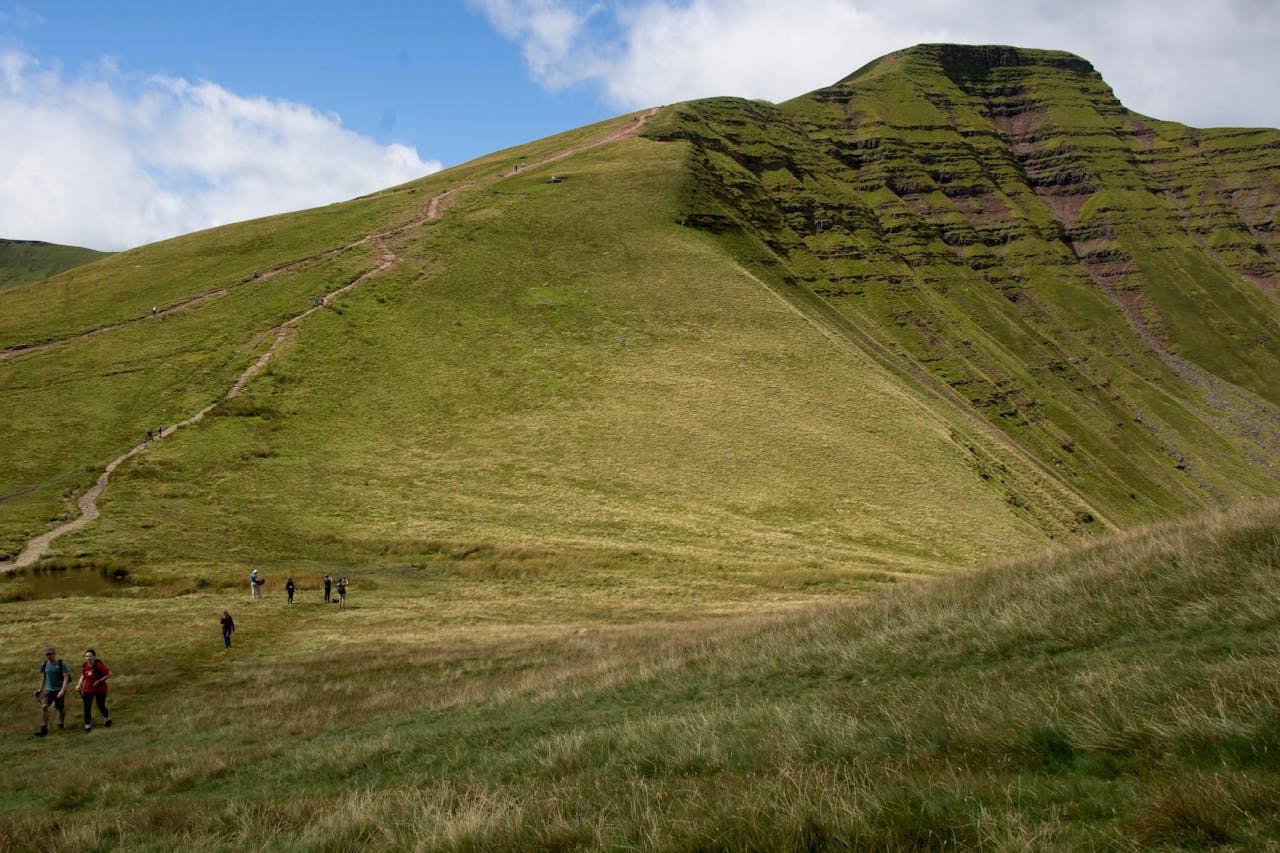 Hikers explore the lush trails of Brecon Beacons in Wales under a vibrant sky.