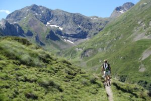 A lone hiker treks through lush green mountains on a sunny day, capturing nature's majesty.